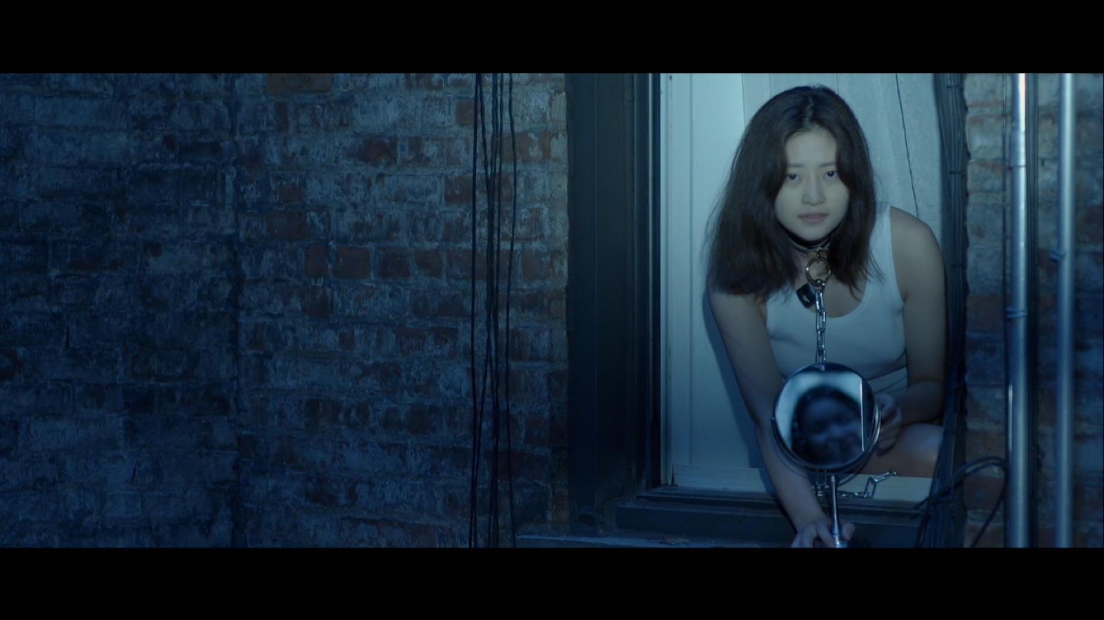 A woman wearing a chain at an apartment window