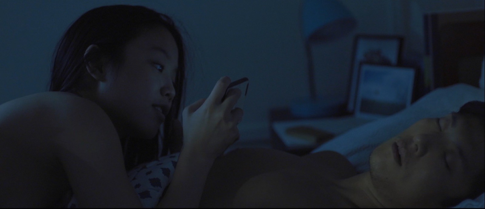 A woman using a phone beside a sleeping man