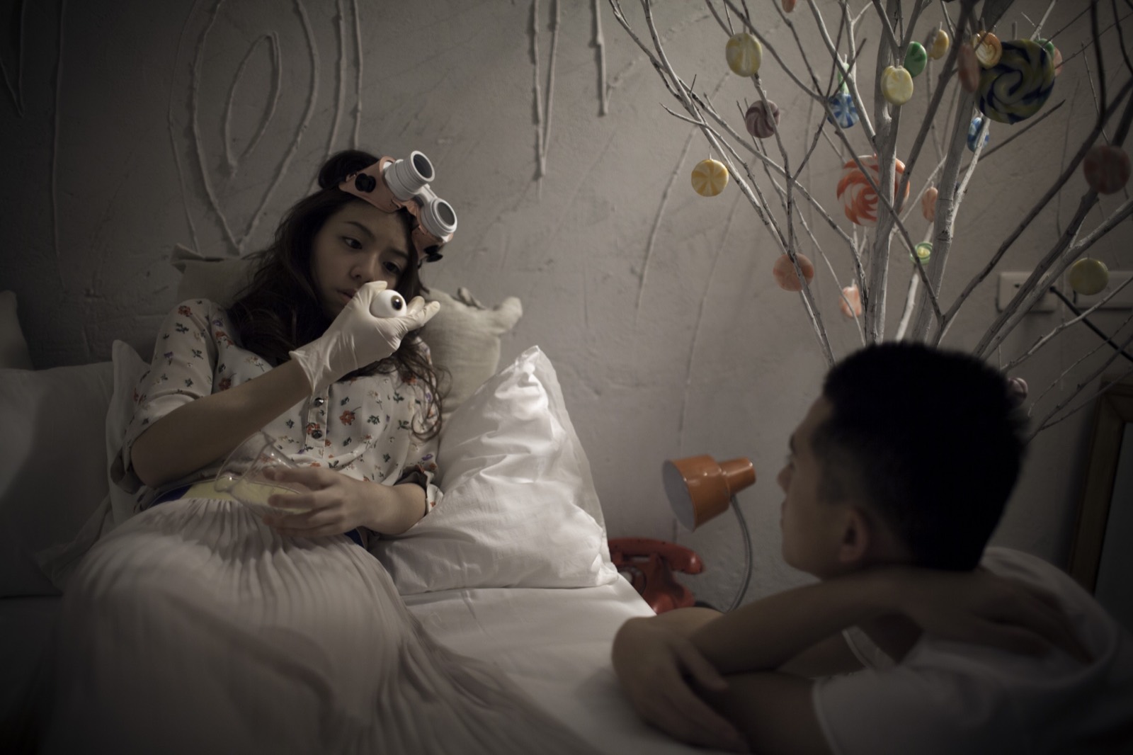 Starry Eyes still: a woman studies an artificial eye beside a candy tree